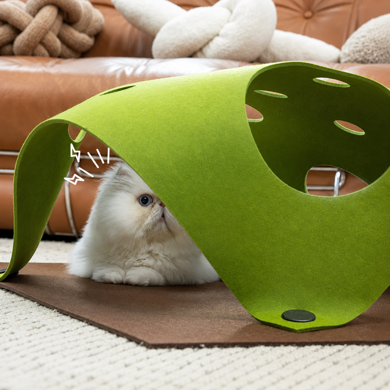 White cat peeking from under the green Felt Play Mat tunnel